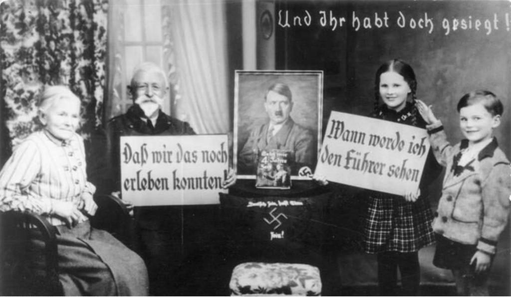 Österreich 1938, Großeltern und Enkel begrüßen mit Propagandaschildern und Hitlerfoto den Einmarsch der deutschen Wehrmacht