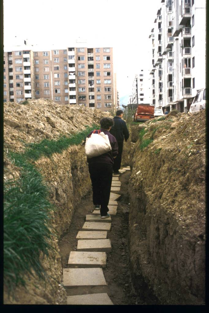 Durch einen angelegten Graben laufen Menschen mit ihren Einkäufen.
