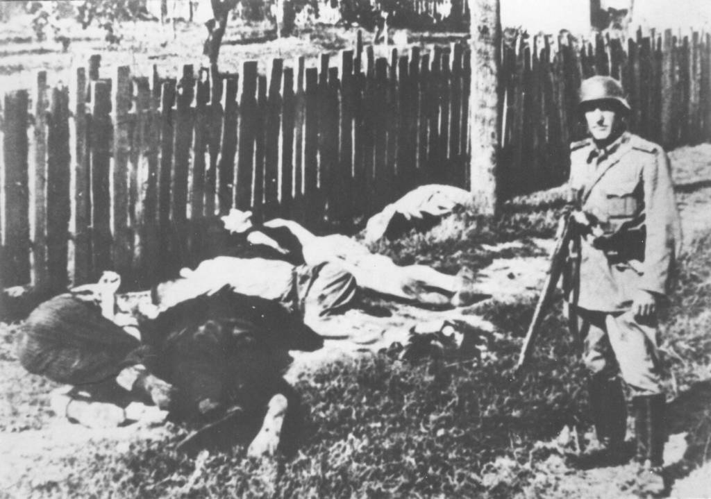 Soldat posiert neben erschossenen Bewohnern des Dorfes Skala.