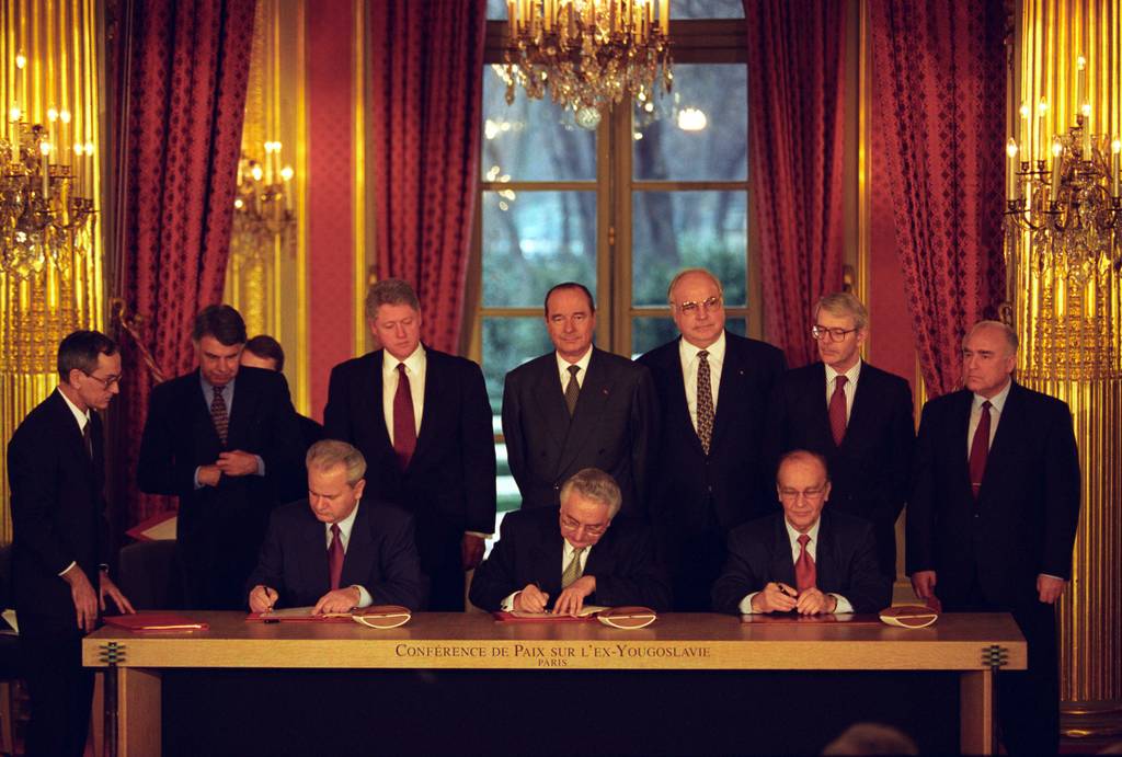 Der serbische Präsident Slobodan Milosevic, der bosnische Präsident Alija Izetbegovic und der kroatische Präsident Franjo Tudjman unterzeichnen das Abkommen von Dayton. Im Hintergrund stehen unter anderem der amerikanische Präsident Jacques Chirac und der deutsche Bundeskanzler Helmut Kohl.